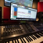 A music studio with a keyboard, monitor and computer.